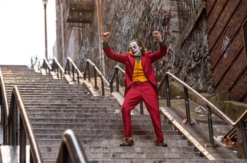 영화 조커(2019) 호아킨 피닉스가 뉴욕 브롱크스 계단에서 붉은 정장을 입고 두 팔을 들어 올리며 춤을 추는 장면