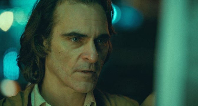 영화 조커(2019) 호아킨 피닉스가 광대 분장 없이 아서 플렉으로서 푸른 조명 아래 냉혹하고 공허한 눈빛으로 정면을 응시하는 장면