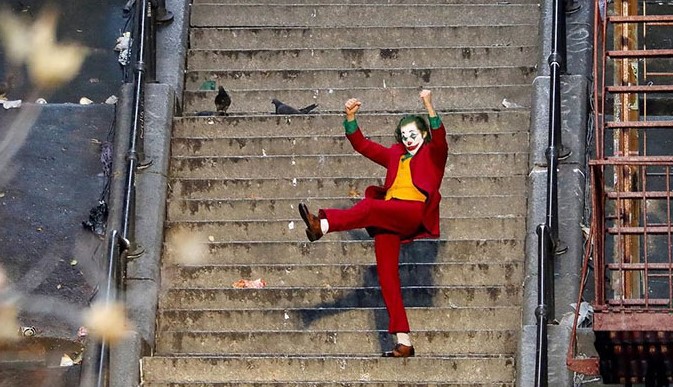 영화 조커(2019) 호아킨 피닉스가 광대 분장과 붉은 정장 차림으로 브롱크스 계단 위에서 한 발을 높이 들어 올리며 춤추는 장면으로 사회적 억압에서 벗어난 해방감을 상징하는 명장면