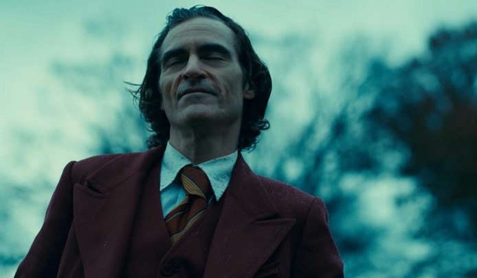 영화 조커(2019) 호아킨 피닉스가 광대 분장 없이 와인레드 재킷 차림으로 눈을 감은 채 희미하게 미소 짓는 장면으로 아서 플렉에서 조커로 내면이 완전히 전환되는 순간을 암시하는 장면