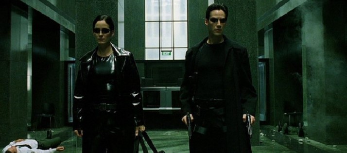 매트릭스에서 검은 가죽 코트를 입은 네오와 트리니티가 총을 들고 건물 내부 홀에 나란히 서 있는 액션 장면, 각성한 두 인물의 결연한 표정