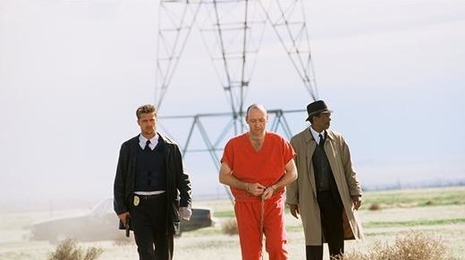 영화 세븐 결말 장면, 주황색 죄수복을 입은 존 도(케빈 스페이시)가 수갑이 채워진 채 밀스(브래드 피트)와 서머셋(모건 프리먼) 사이에서 송전탑이 보이는 황량한 벌판을 걸어가는 장면