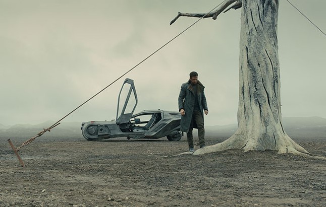 블레이드 러너 2049 스틸컷 — 황량한 벌판에 홀로 선 K(라이언 고슬링)와 죽은 나무, 스피너