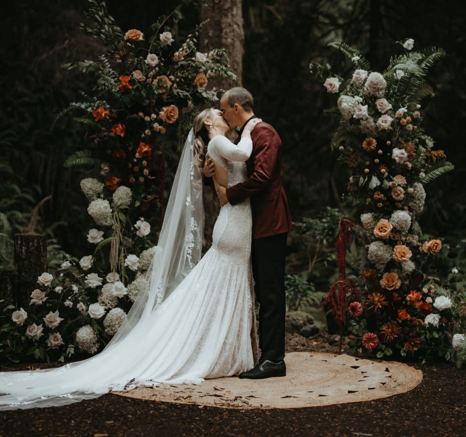 Bride and groom kissing at the altar beneath a dramatic standing floral arch
