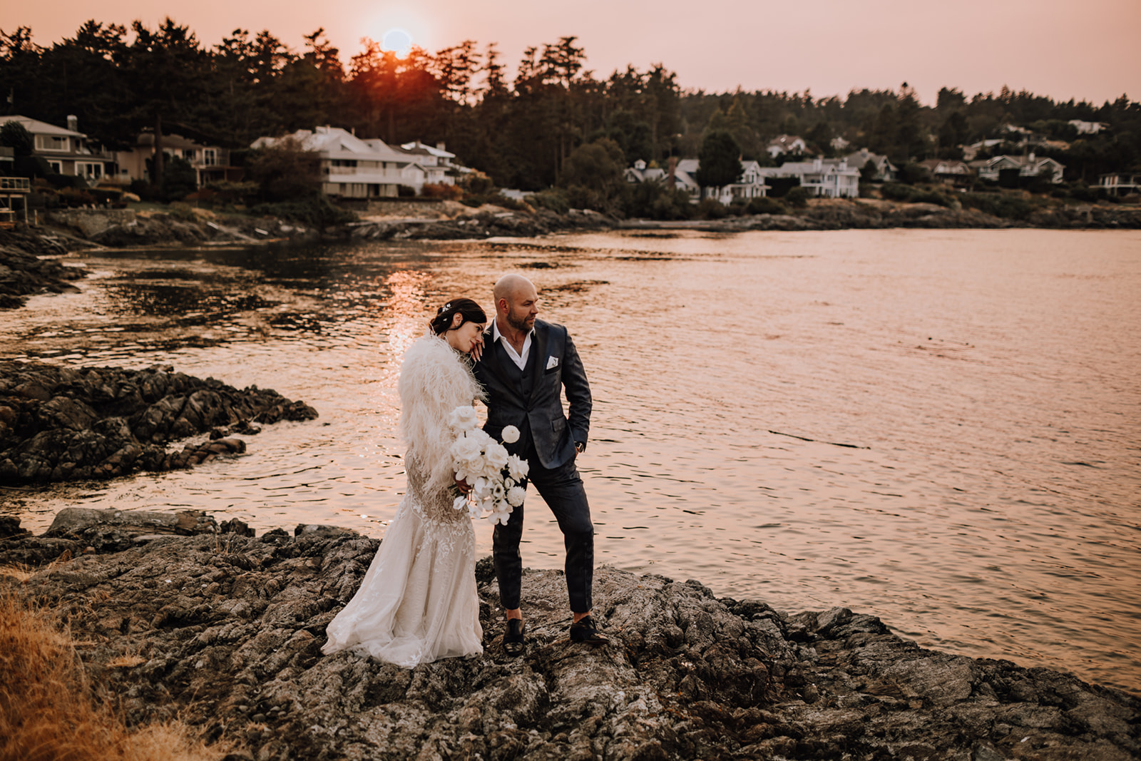 Groom and Bride with white monochrome bouquet in hand, standing on rocks alongside the ocean