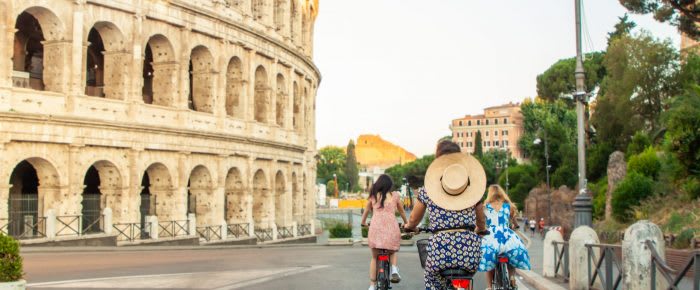 Three happy young women friends tourists with bikes at Colosseum in Rome, Italy at sunrise.