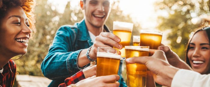 Group of multi ethnic friends having backyard dinner party together - Diverse young people sitting at bar table toasting beer glasses in brewery pub garden - Happy hour, lunch break and youth concept