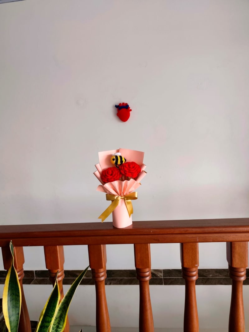 Ramo artesanal Nuditos: Dos rosas rojas tejidas a crochet acompañadas de una pequeña y tierna abejita amigurumi amarilla y negra, envuelto en papel coral con un lazo dorado vibrante.