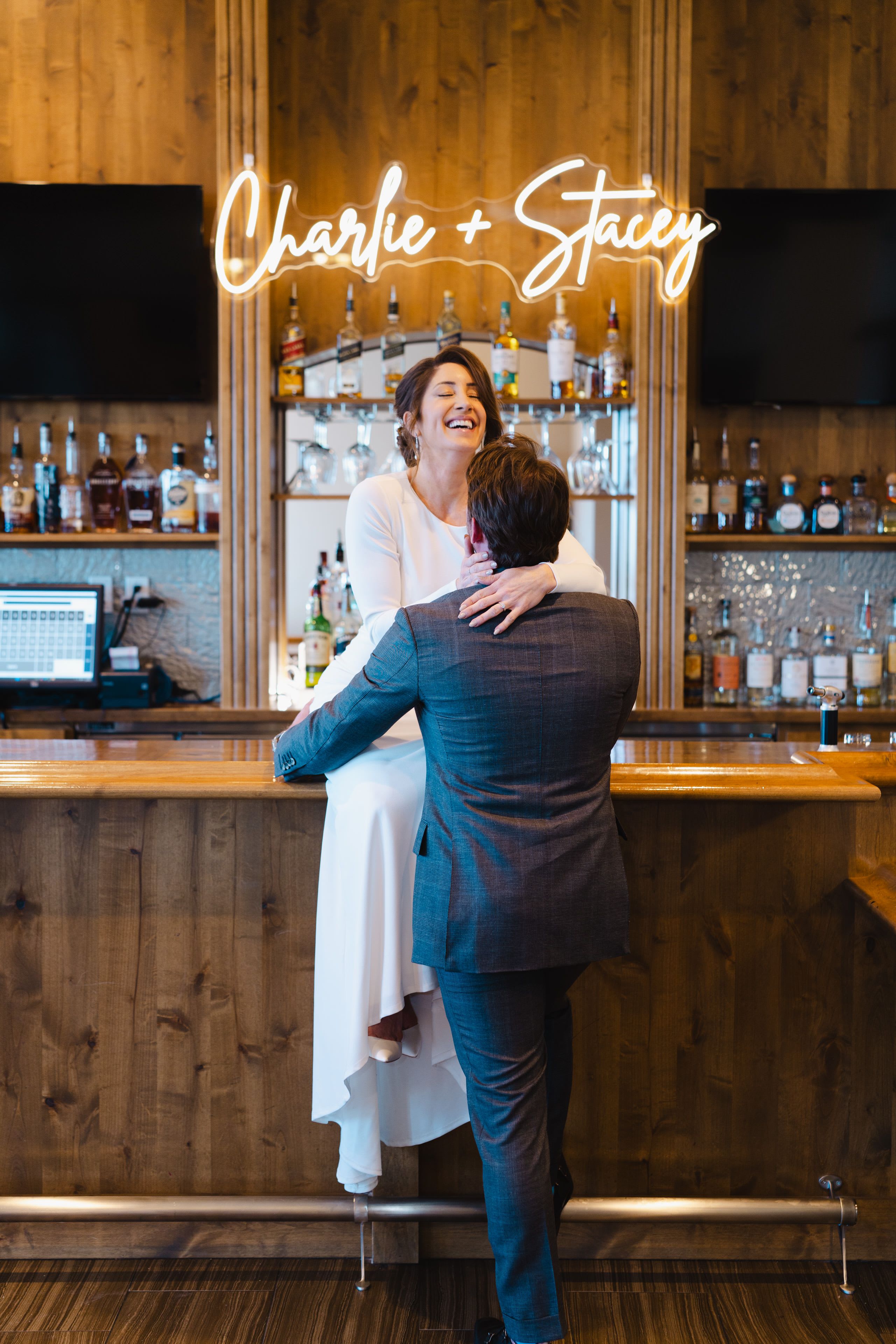 wedding couple sitting on a bar below a neon sign