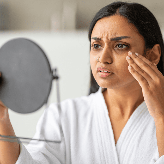 A woman concerned while examining her face in a handheld mirror showing signs of body dysmorphic disorder
