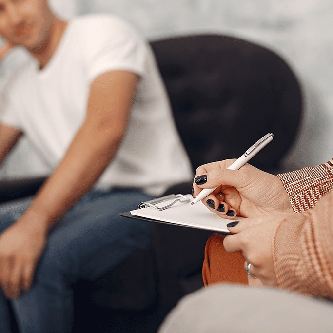 A calm counselling session where a professional listens and takes notes while a person speaks. The setting reflects trust, emotional safety, and the importance of understanding human behaviour through guided conversation and professional support.