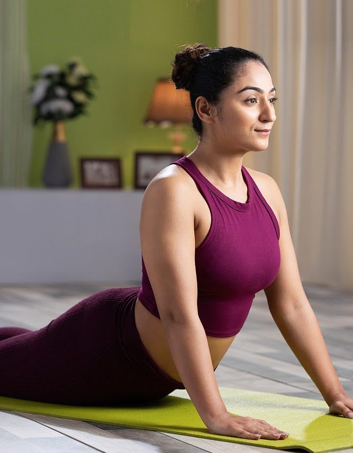Woman practising yoga therapy in a gentle cobra pose on a yoga mat indoors, focusing on mindful movement, posture, and relaxation.
