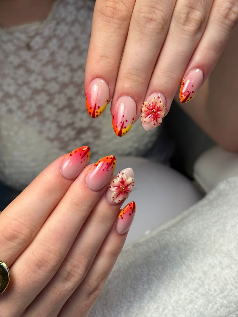 Nagels met oranje en gele tips, rode spikkels en een 3D-bloem