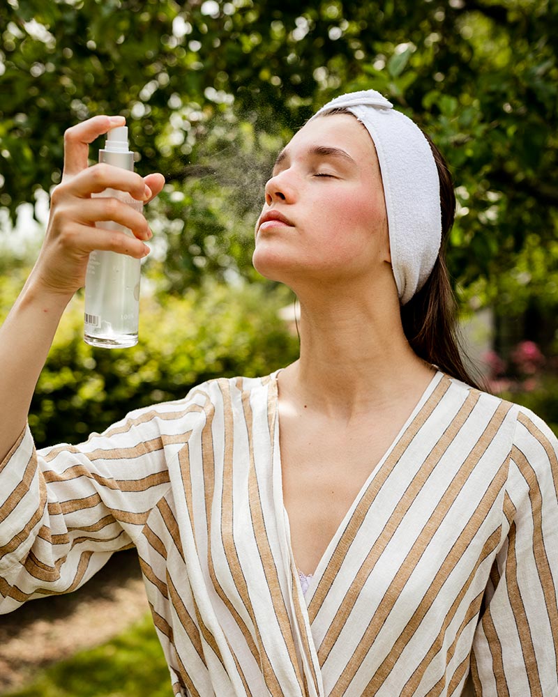 Vrouw met gesloten ogen gebruikt een natuurlijke skinspray in de tuin