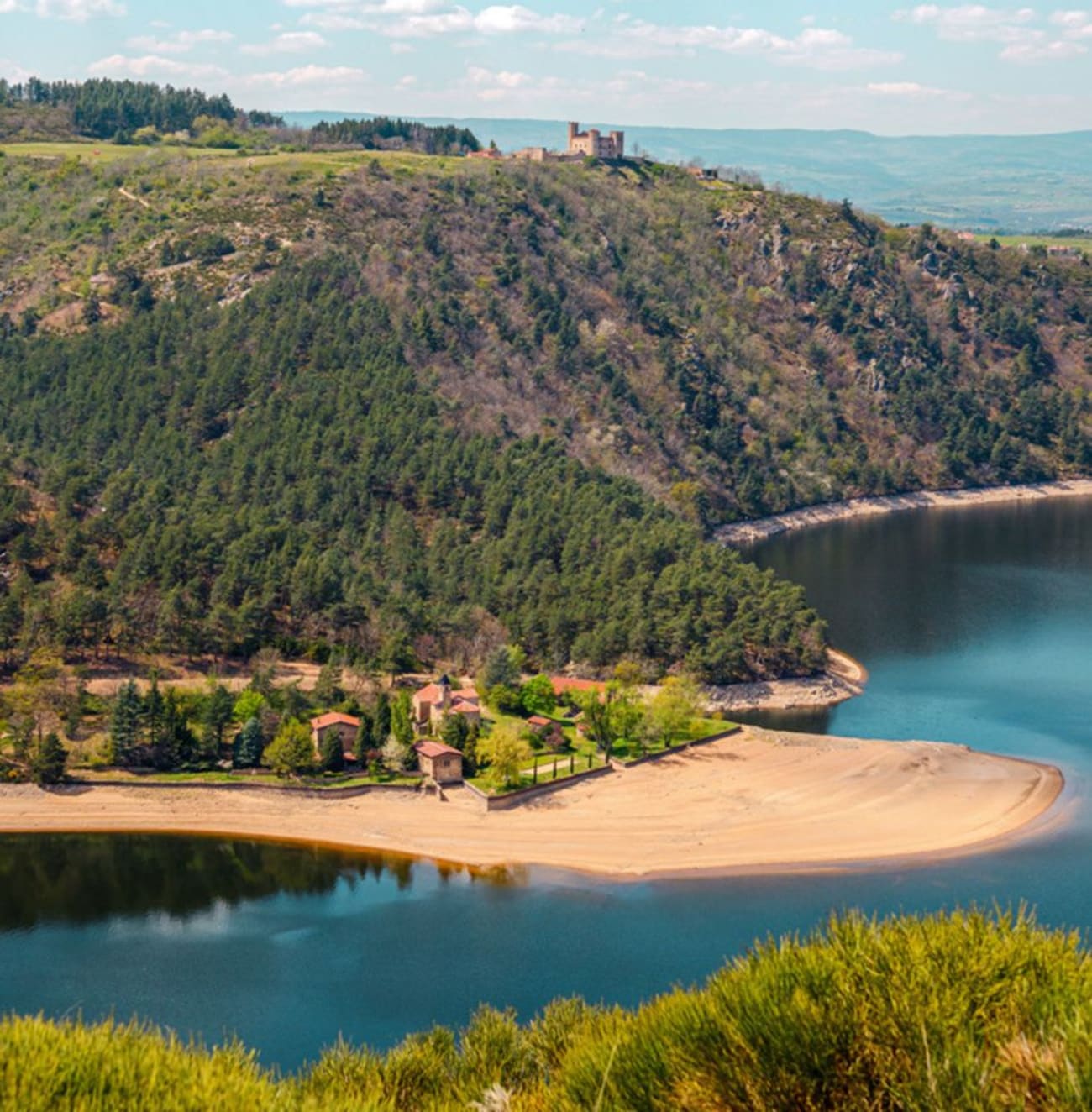 Panorama sur la rive gauche des Gorges de la Loire : végétation, lac de Grangent et château au loin.