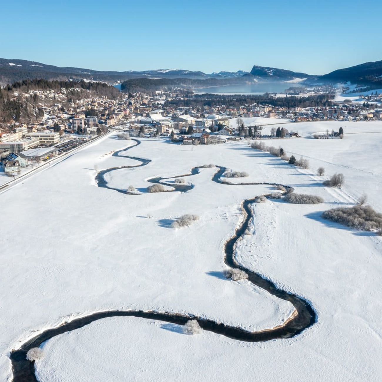 Randonnée raquettes Jura : étendue de neige et rivière serpentant près d'une ville