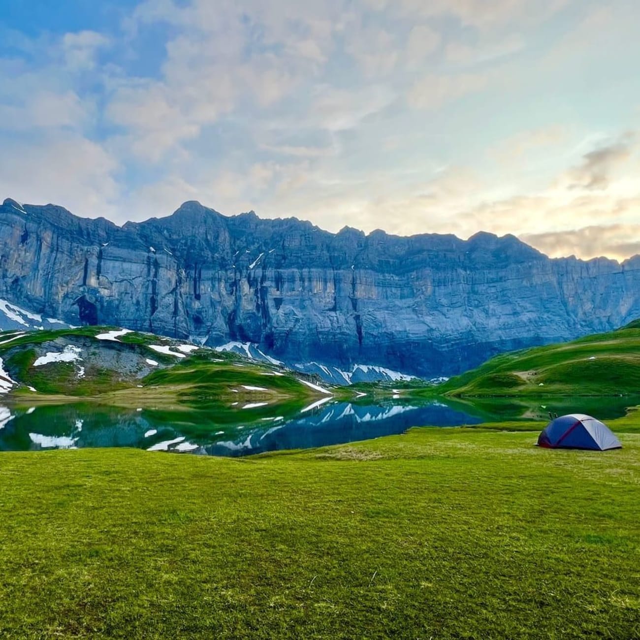 Randonnée lac d'Anterne : tente sur pelouse au bord d'un lac, au pied de montagnes acérées avec un peu de neige