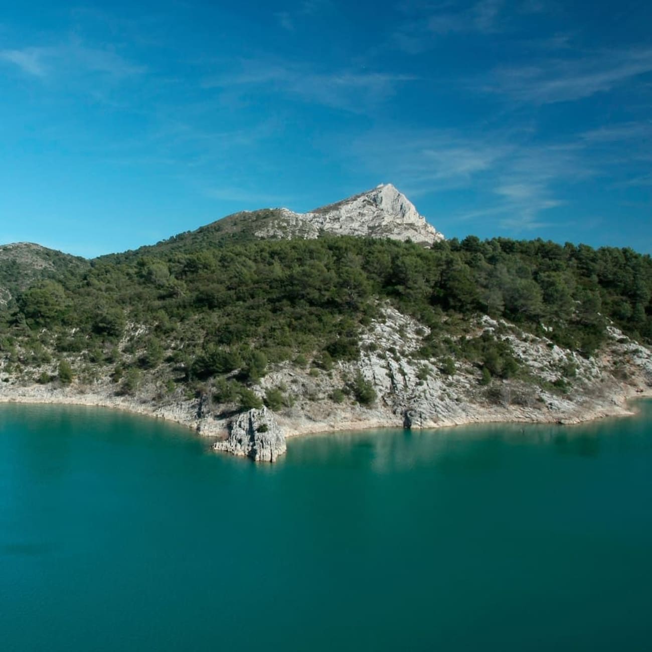 Randonnée lac de Bimont : eau bleue bordée par roche et buissons verts avec sommet pointu au fond