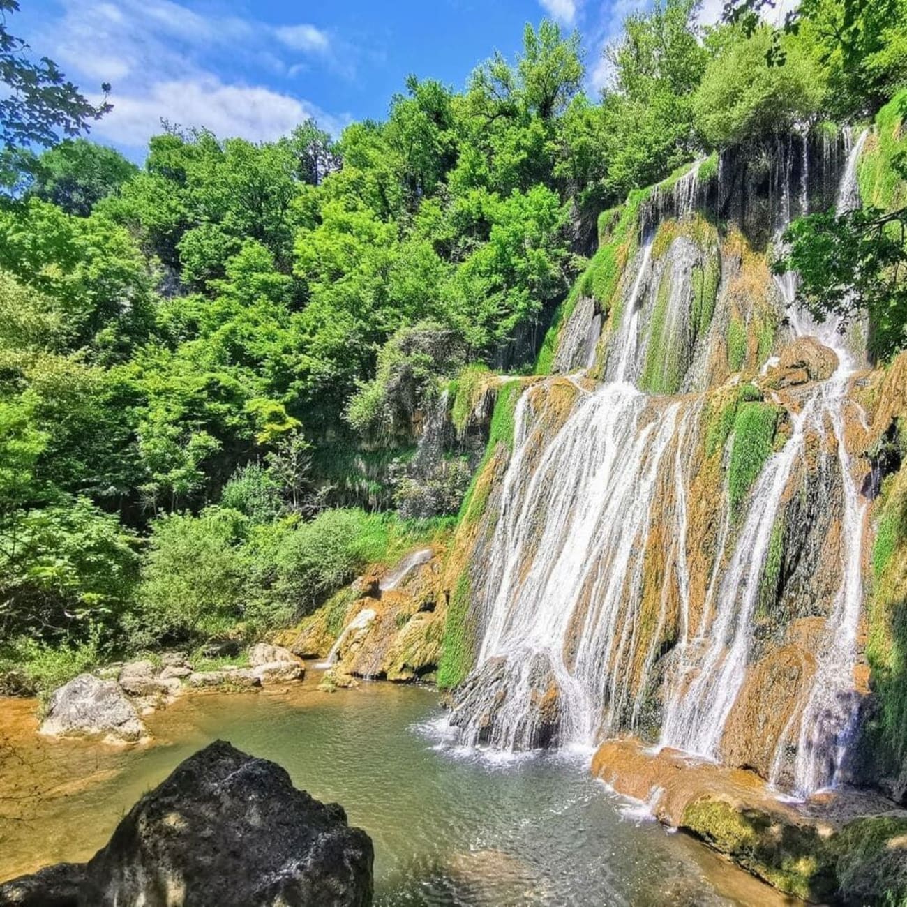 Randonnée cascades Ain : chute d'eau dégringolant sur roche végétalisée avec bassin à son pied