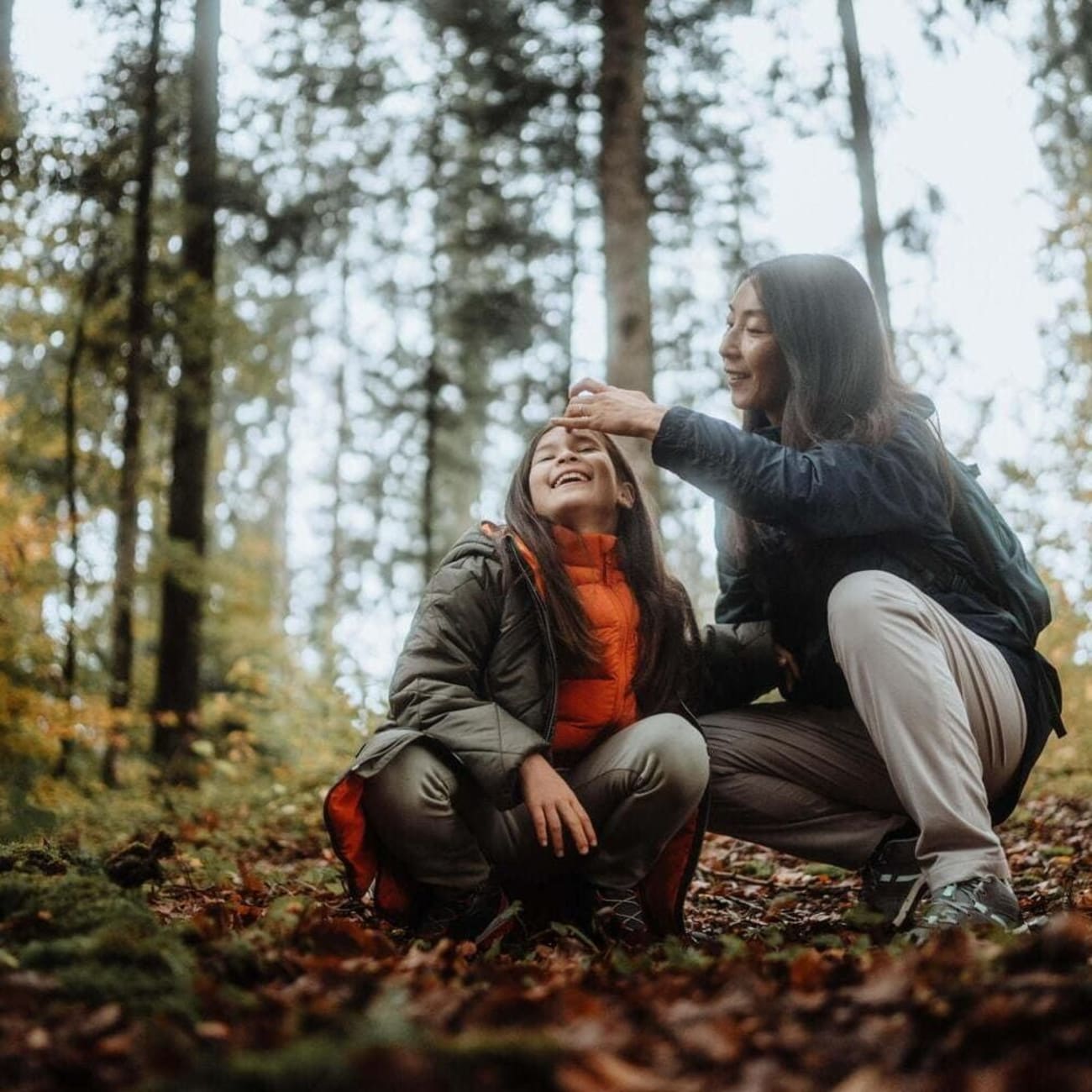 Randonnée automne : femme avec un enfant agenouillés dans les feuilles mortes et entourés d'arbres
