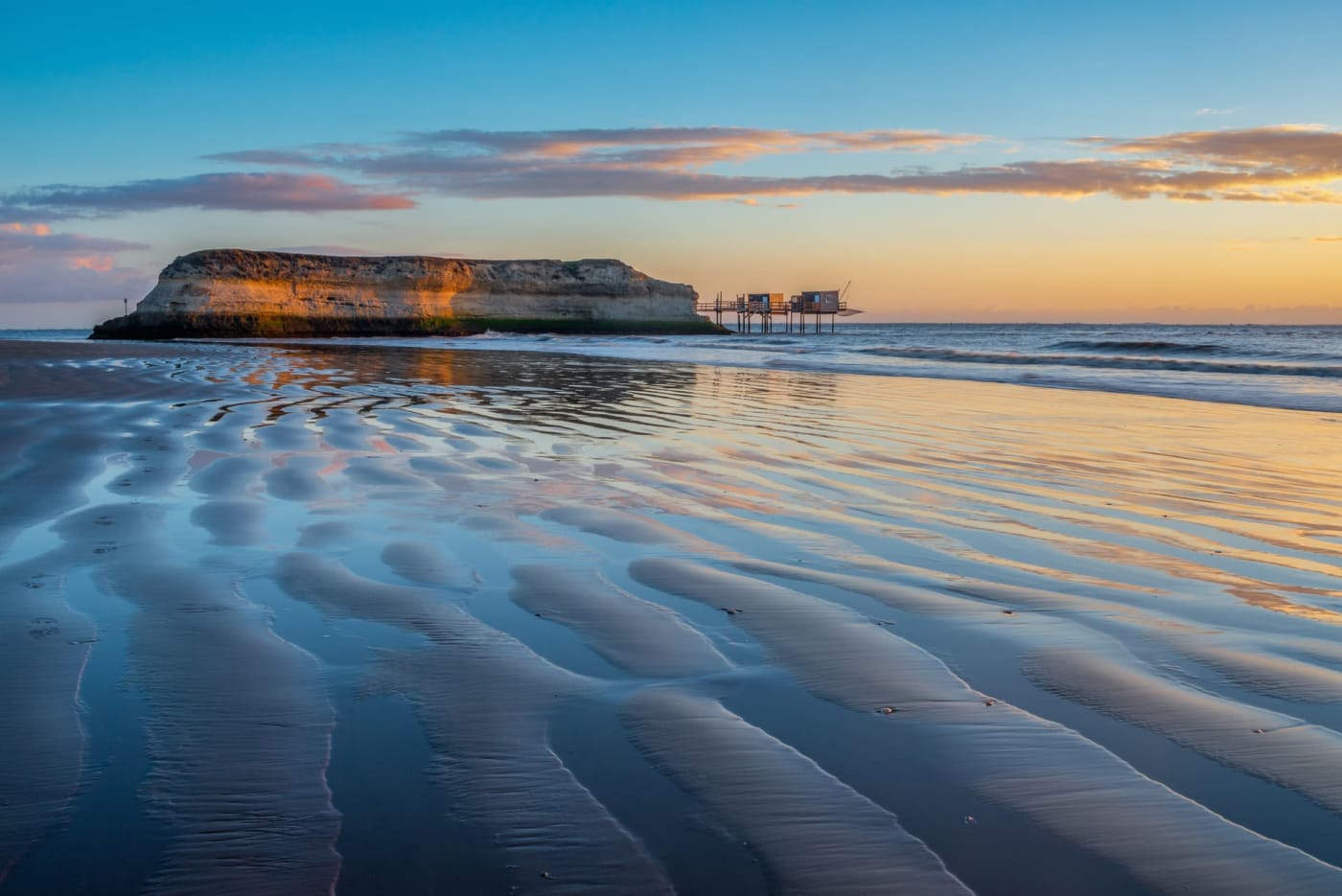 Sable à marée basse, falaise au milieu de la mer avec cabanes de pêcheurs