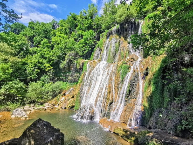 Randonnée cascade de Glandieu : chutes d'eau coulant sur la roche entourée d'arbres verts