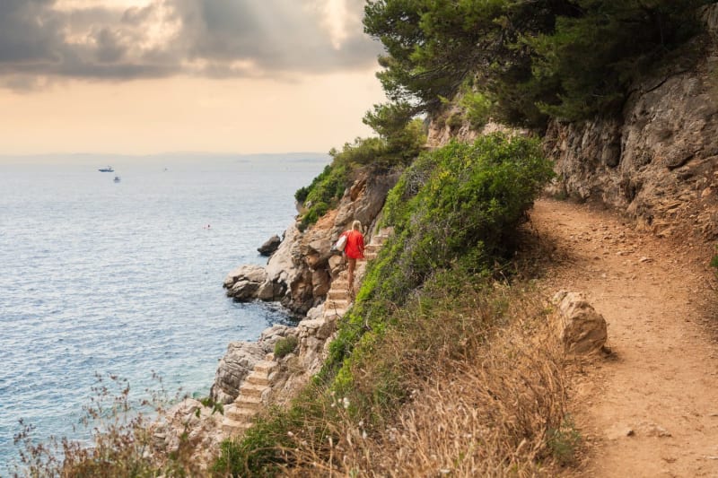 Randonnée sentier du littoral Saint-Jean-Cap-Ferrat : femme habillée en rouge qui monte des marches le long de la mer