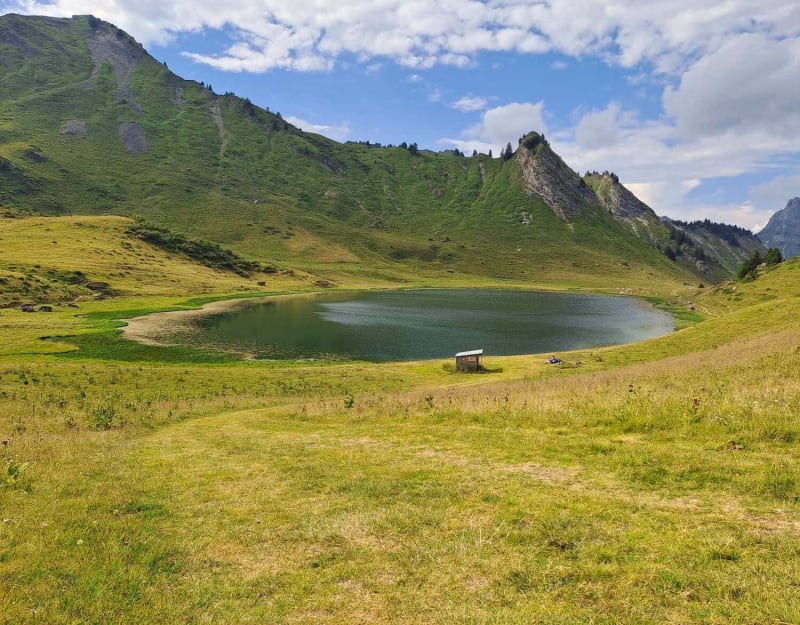 Randonnée lac de Roy : lac rond entouré d'herbe verte et de montagnes verdoyantes