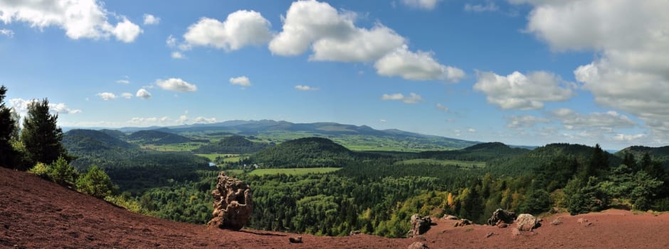 Randonnée puy de la Vache : panorama chaîne des Puys, sable rouge, scories, volcans verts, ciel bleu et nuages blancs