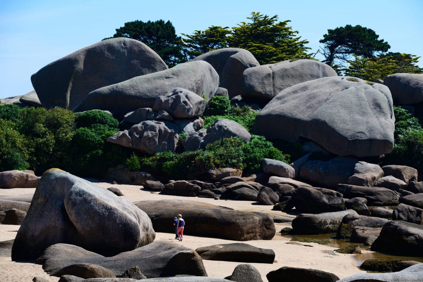 Randonnée île Renote : personnes marchant dans les chaos granitiques éparpillés sur la plage et dans la végétation