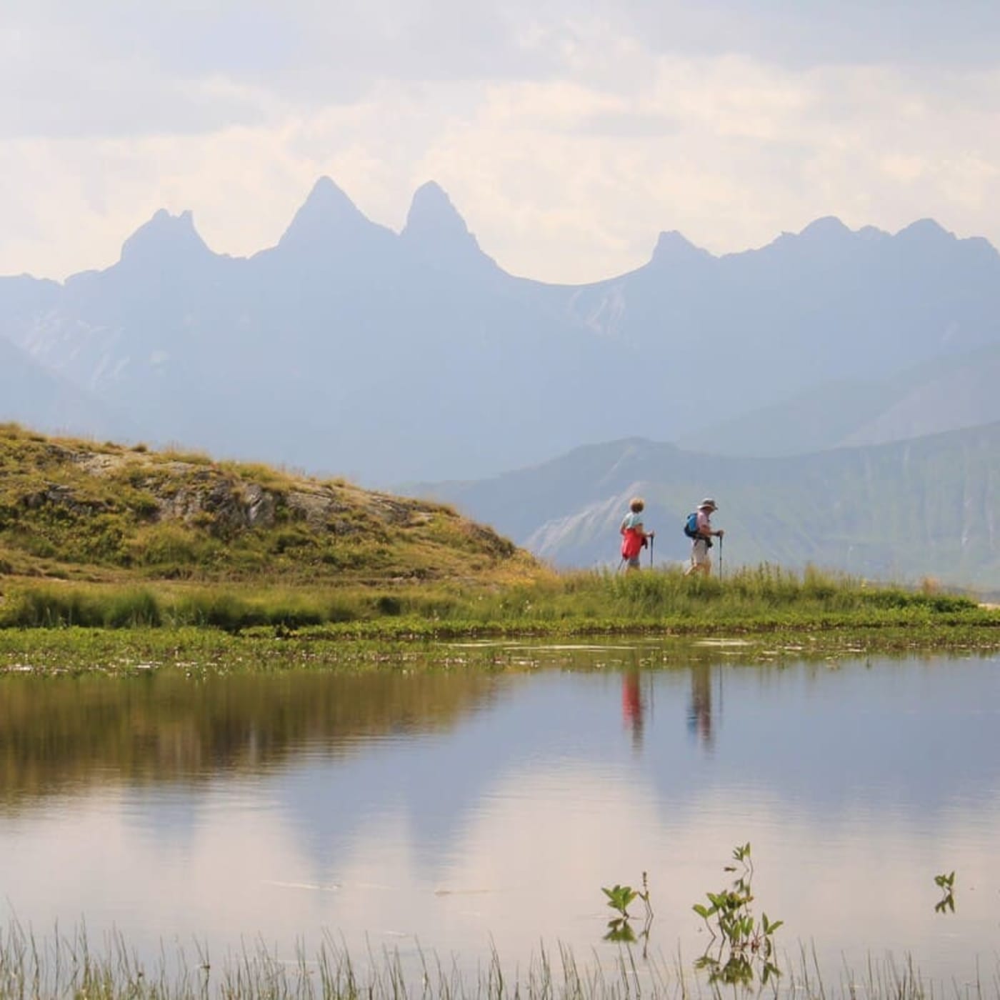 Randonnée lac Guichard : 2 randonneurs se promènent le long du lac où se reflètent les montagnes