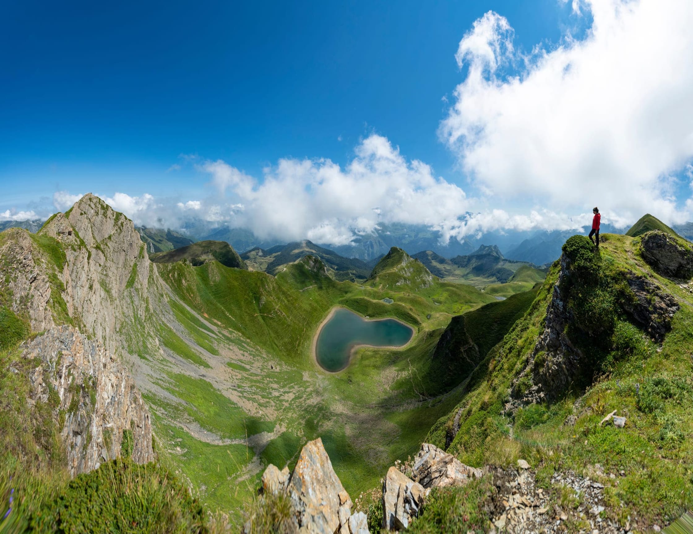 Randonnée lac du Montagnon : personne qui regarde un lac en forme de cœur au milieu des montagnes verdoyantes