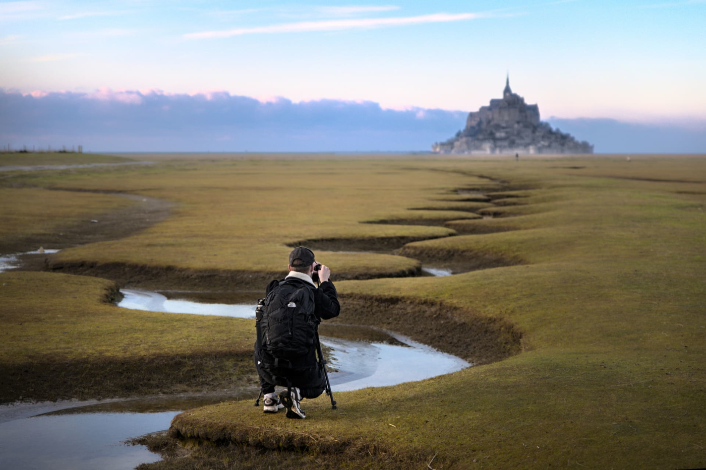 Homme prenant une photo du mont Saint-Michel près de l'eau serpentant vers le mont