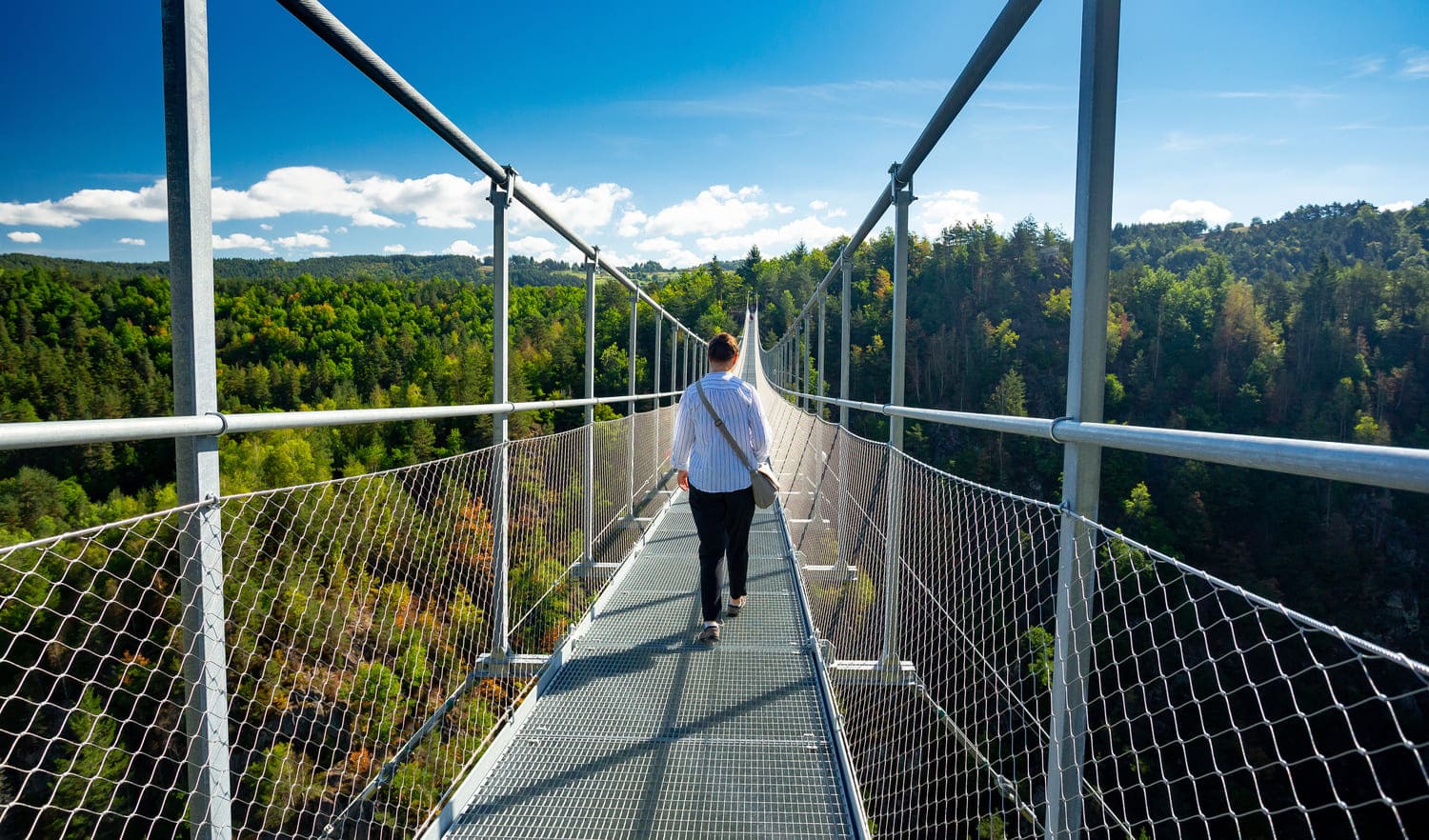 Une randonneuse traverse la passerelle des gorges du Lignon