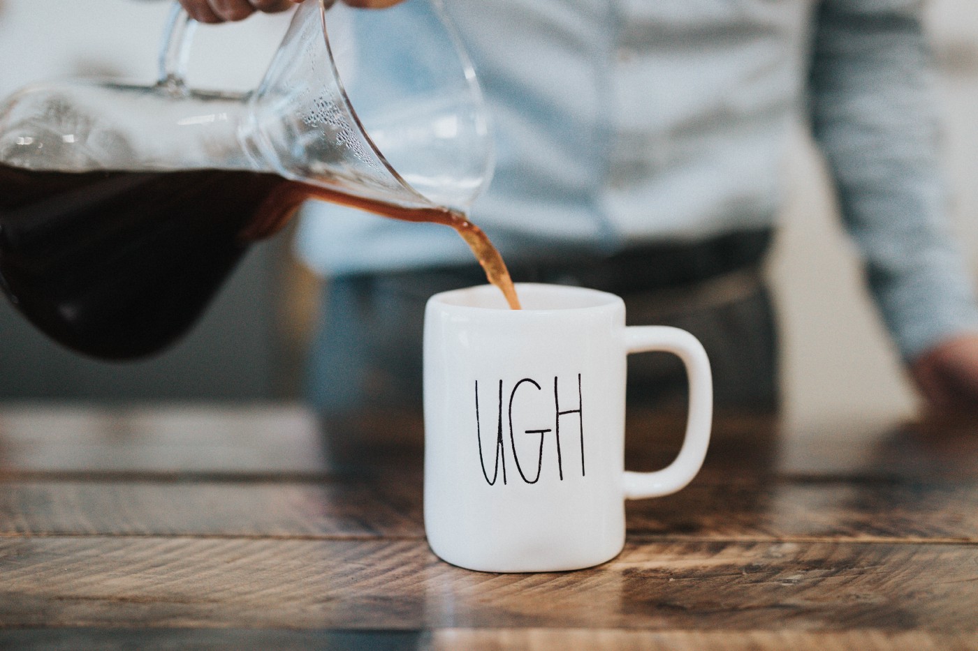 Man pouring coffee into white mug with UGH written on it