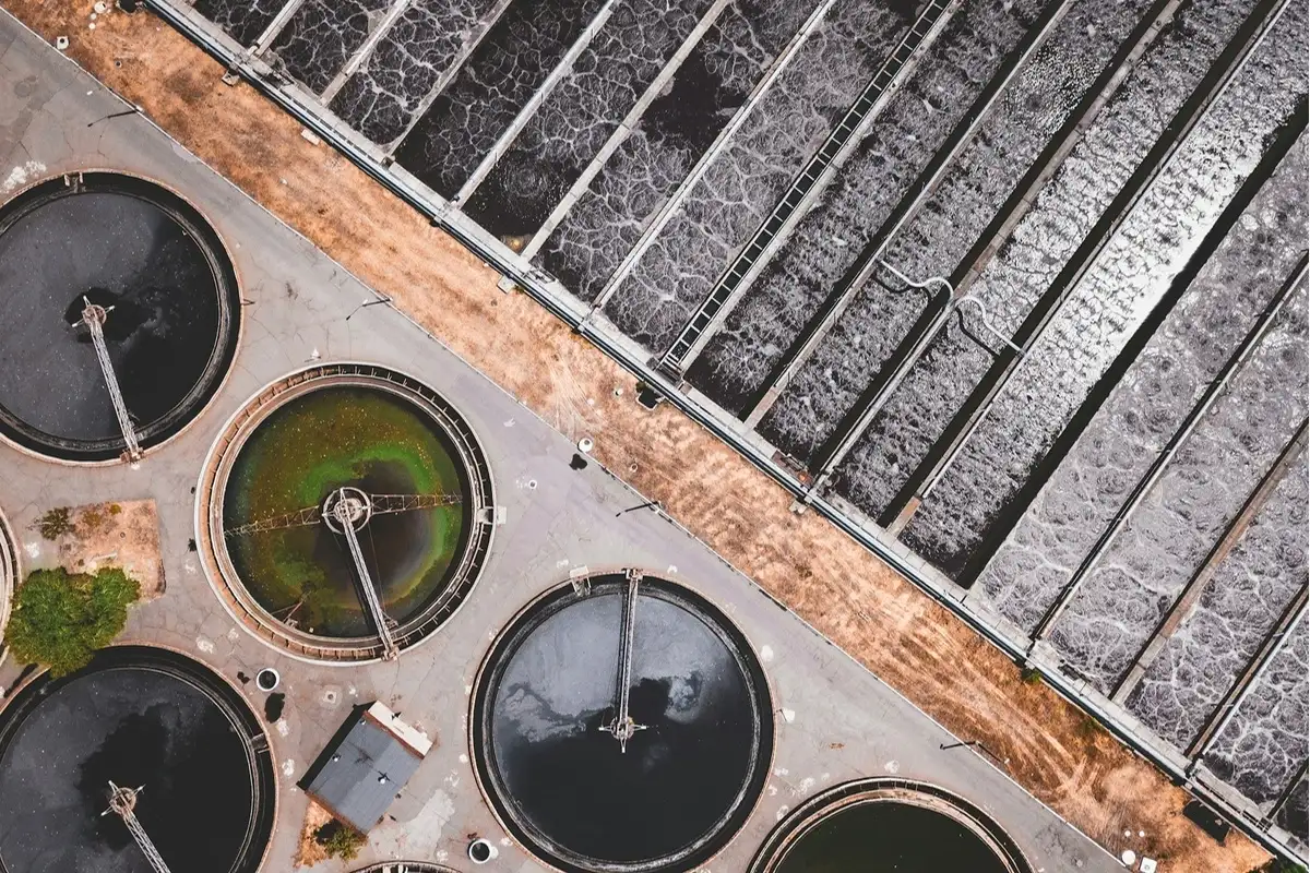 Aerial view of a wastewater treatment plant with circular clarifiers and rectangular aeration tanks.