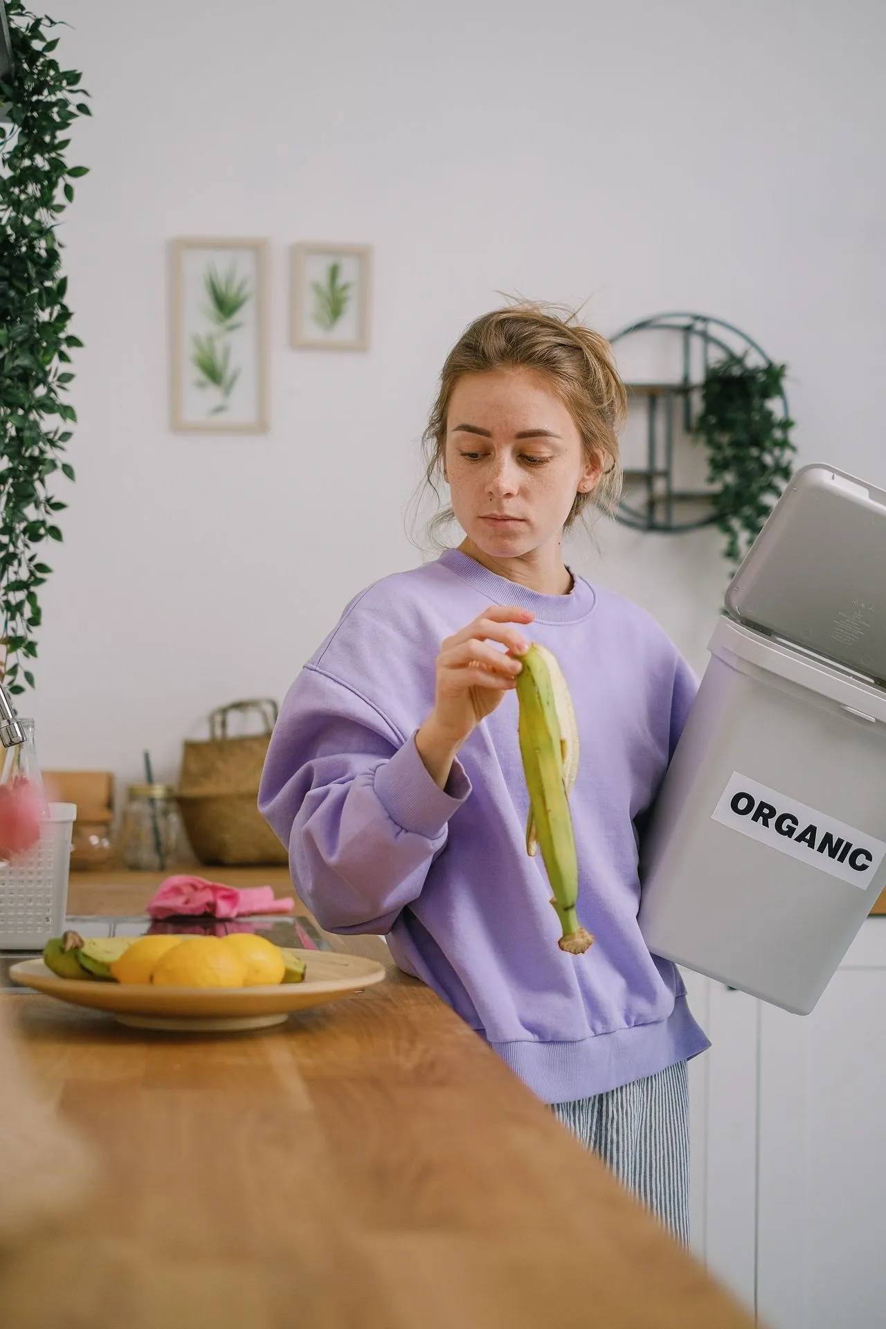 Woman disposing banana peel into an organic waste bin