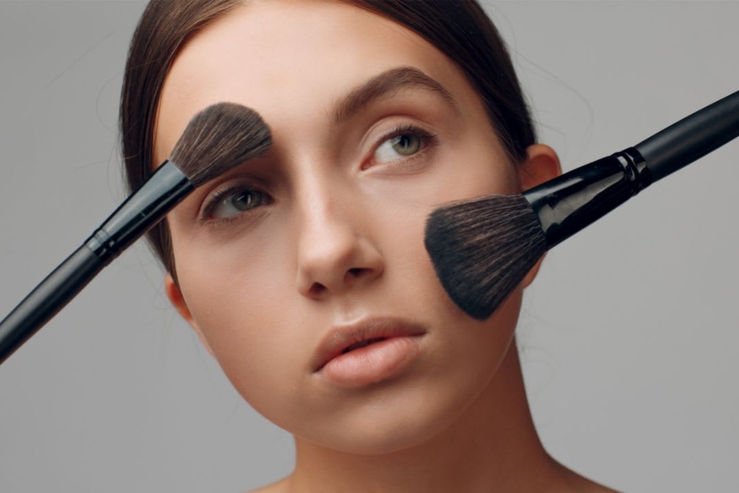 Imagem mostra mulher com estilo de maquiagem natural e pincèis no seu rosto.