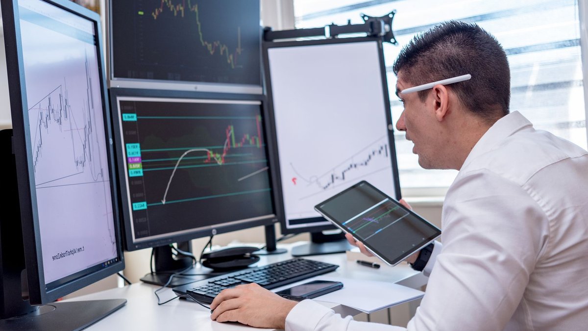 A man analyzing stock market graphs on multiple screens at a workstation.