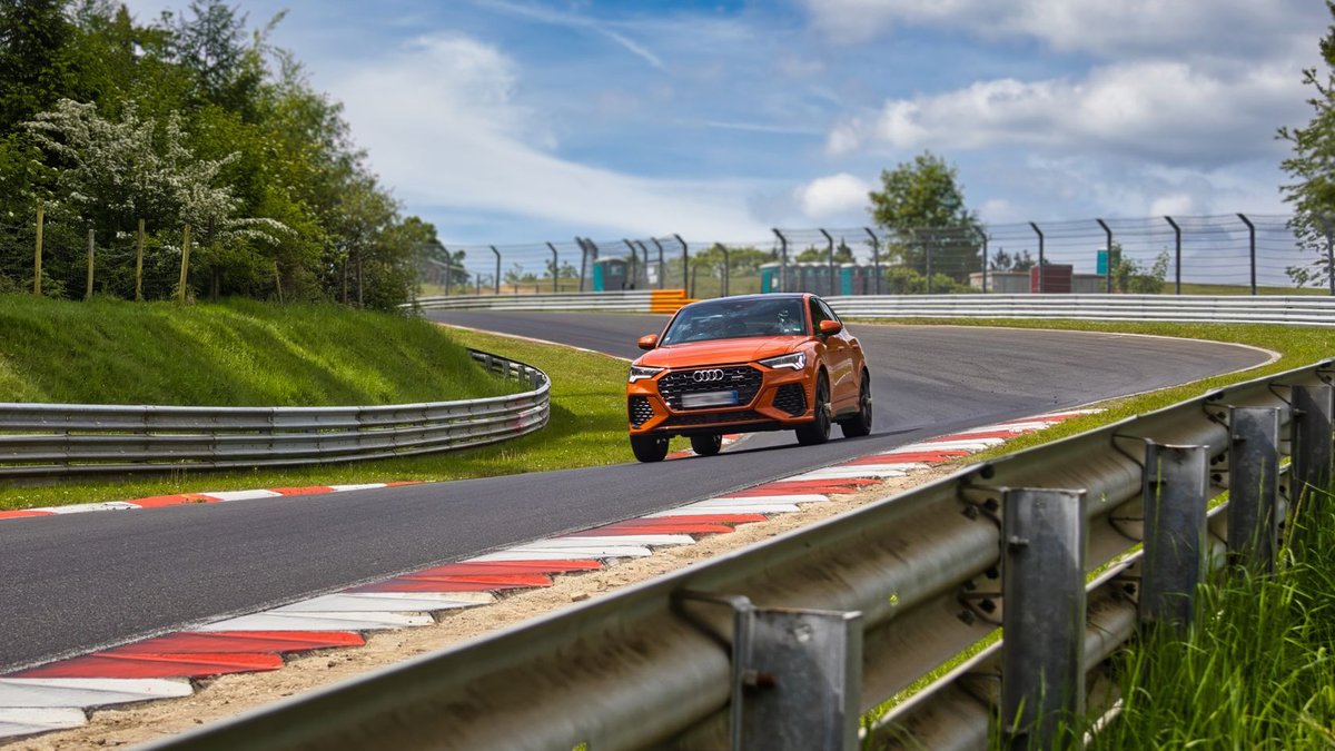 Orange sports car racing on Nürburgring circuit under cloudy skies.