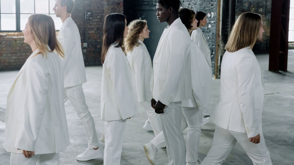 A diverse group of people in matching white outfits walking indoors, exuding unity and harmony.