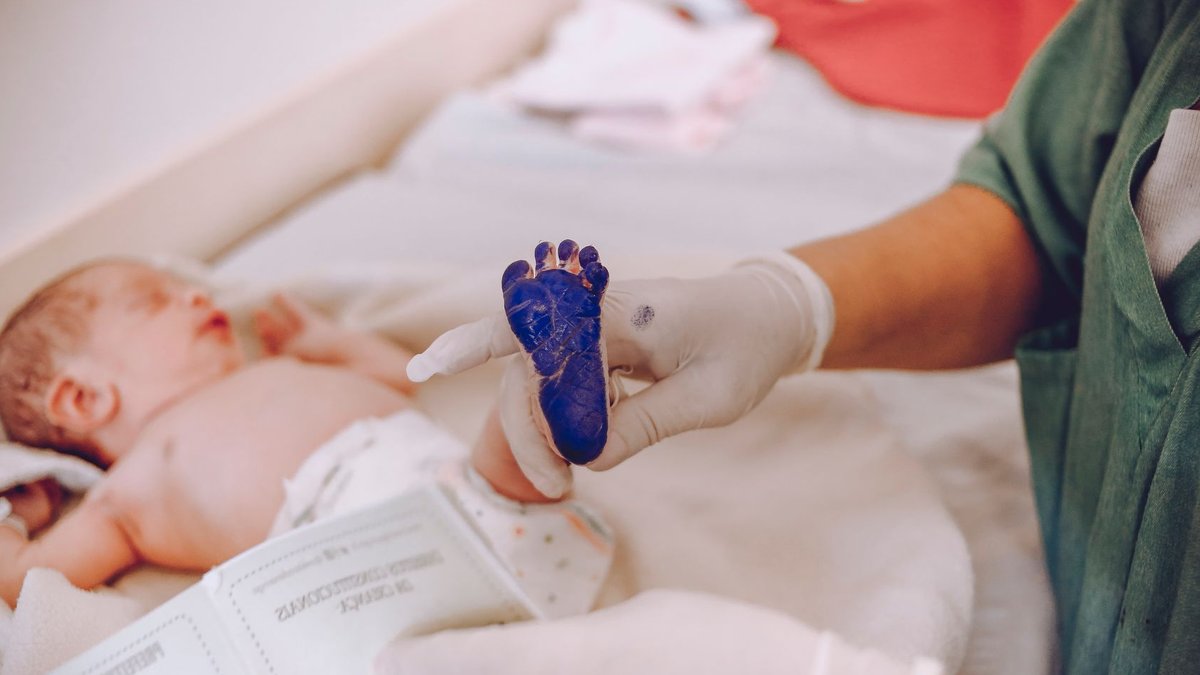 Medical professional taking footprint of a newborn baby in hospital setting.