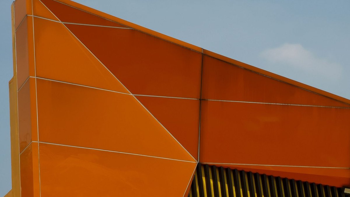 Berlin restaurant adopts quirky design with intentional imperfections Close-up view of a modern building facade with orange geometric shapes and architectural details.