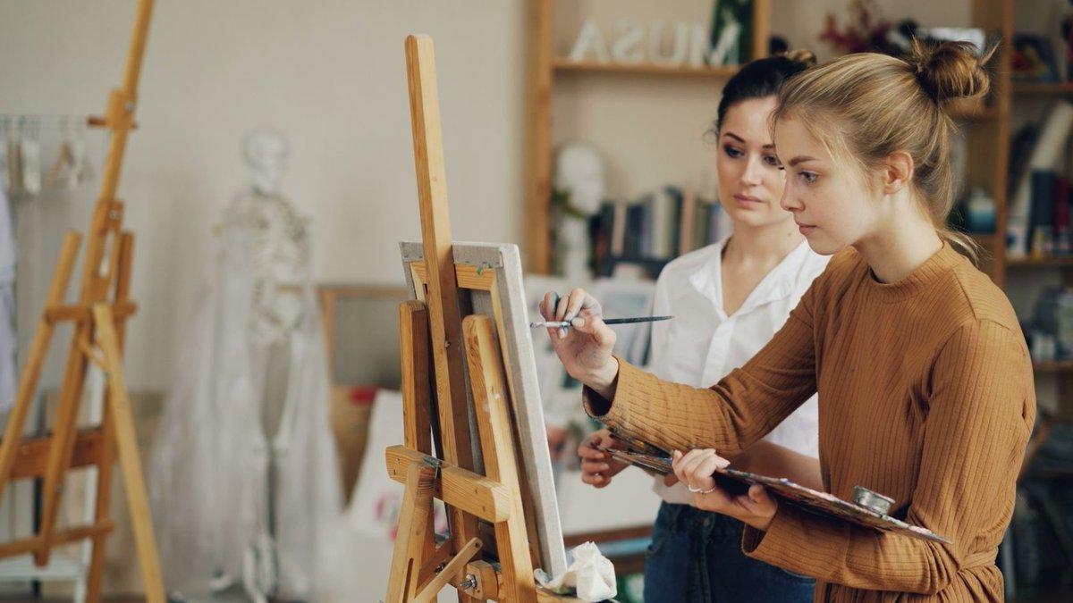 Two women focused on painting at easels in a creative art studio.