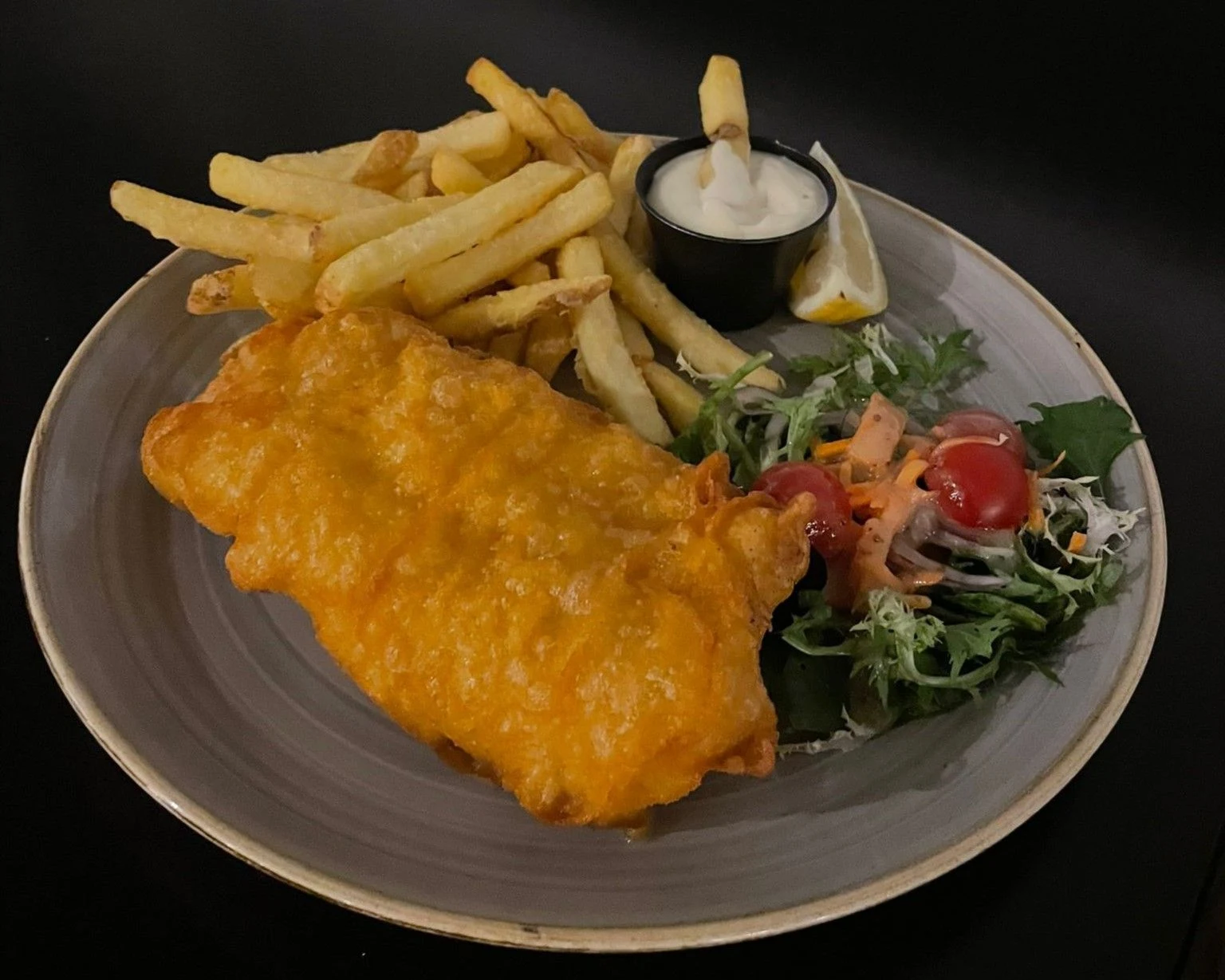 A restaurant-style serving of fish and chips with salad, lemon and sauce. 