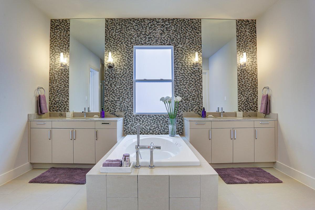 eggersmann-designed luxury bath featuring a garden bath tub in between twin vanities in a light taupe laminate decor finish with a mosaic tile floor-to-ceiling backsplash in a home in royal oaks courtyard villas in houston