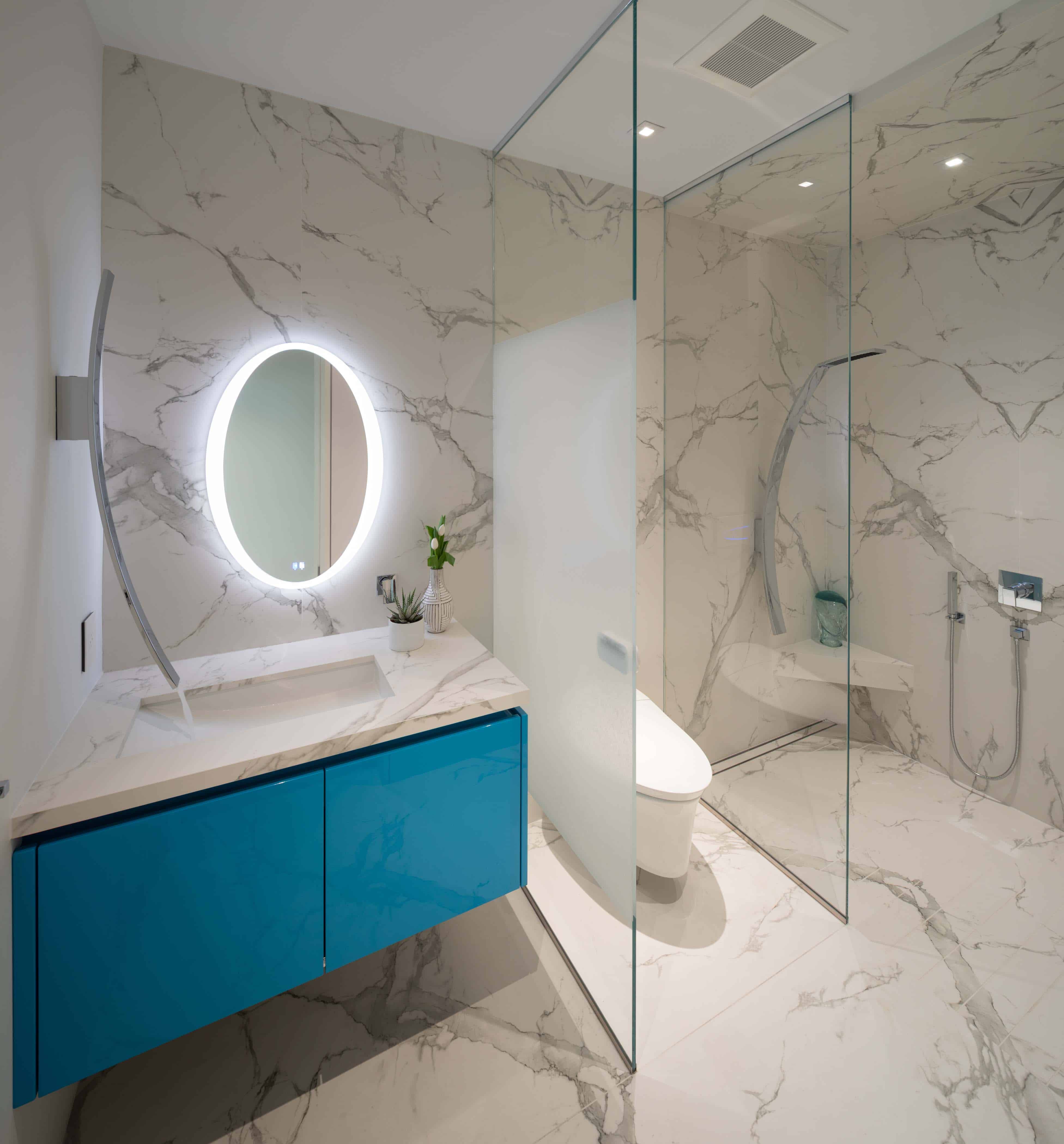 standout turquoise gloss vanity with backlit mirror abuts a water closet and shower with partially sandblasted glass walls in an eggersmann-designed bathroom