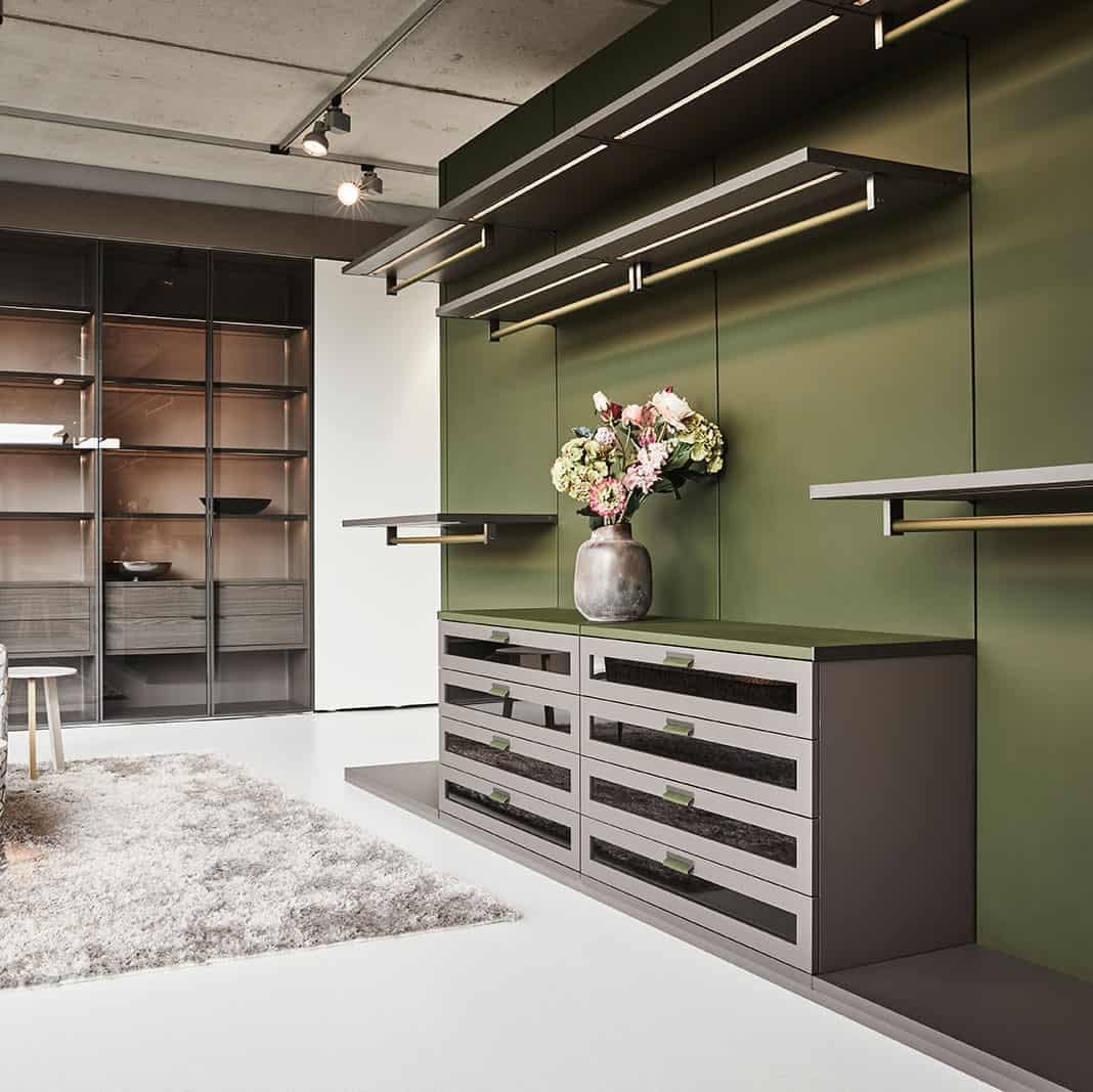 custom luxury walk-in closet with a green accent wall and warm wood touches by schmalenbach designed by eggersmann