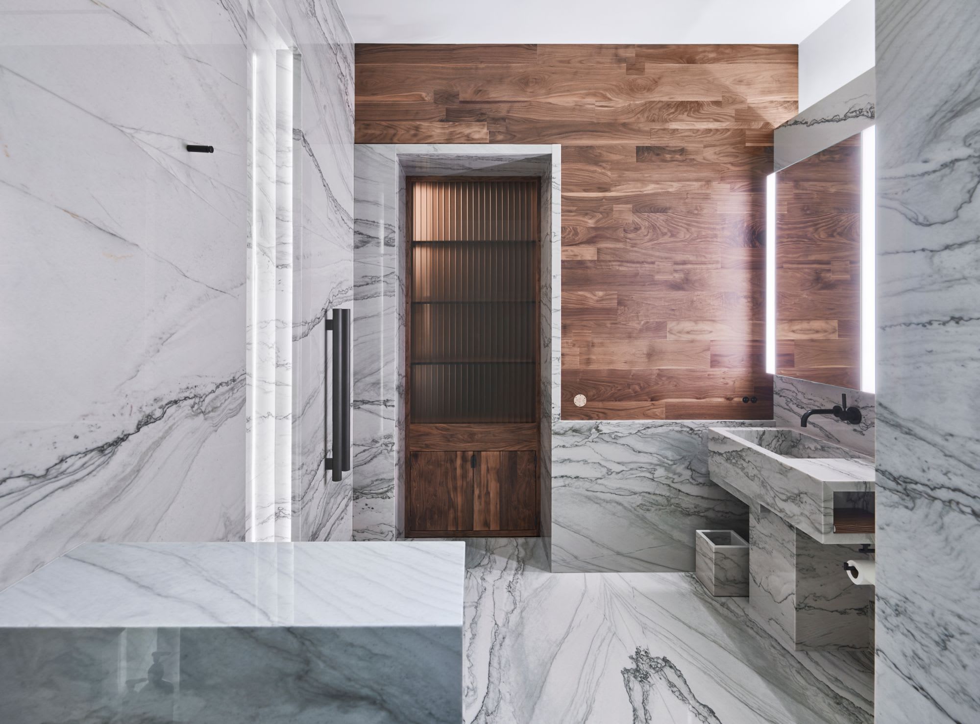luxury bathroom featuring classic white marble and a warm wood plank accent wall inside a penthouse of the arabella luxury high rise in houston