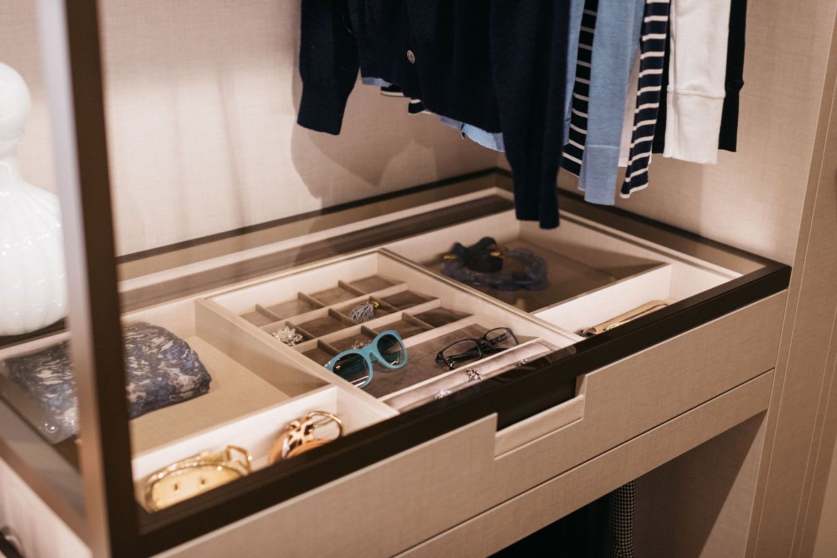 glass-top sunglass and fashion accessories display case below hanging clothes storage